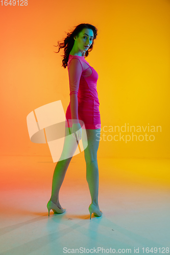 Image of Beautiful seductive girl in fashionable, romantic outfit on bright gradient yellow-orange background in neon light