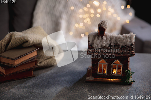 Image of Winter house miniature illuminated and books on grey and white background. The concept of home atmosphere and comfort.