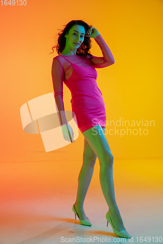 Image of Beautiful seductive girl in fashionable, romantic outfit on bright gradient yellow-orange background in neon light