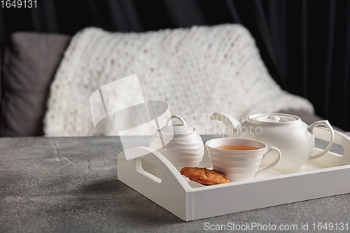 Image of White wooden tray with tea set and miniature of house isolated on grey and white background.