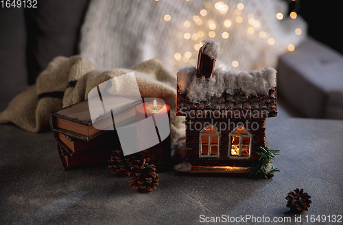 Image of Winter house miniature illuminated and books on grey and white background. The concept of home atmosphere and comfort.