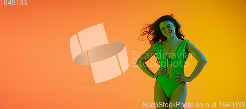 Image of Half-length portrait of beautiful seductive girl in fashionable green swimsuit on bright gradient background in neon light