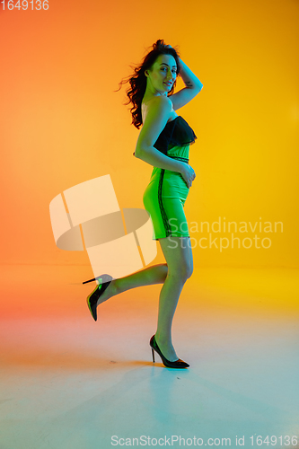 Image of Beautiful seductive girl in fashionable, modern outfit on bright gradient yellow-orange background in neon light