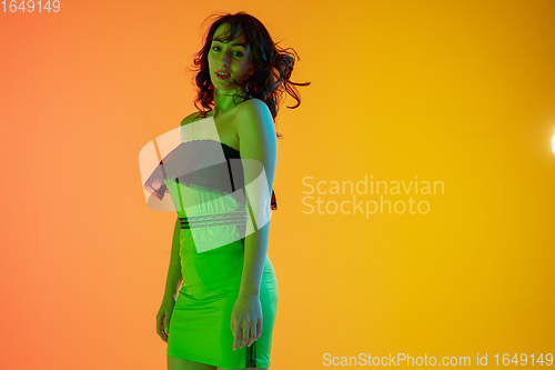 Image of Half-length portrait of beautiful seductive girl in fashionable, modern outfit on bright gradient background in neon