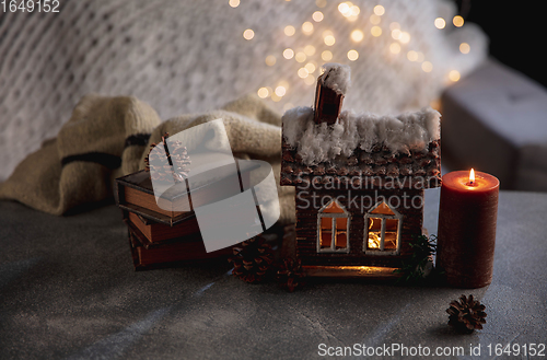 Image of Winter house miniature illuminated and books on grey and white background. The concept of home atmosphere and comfort.
