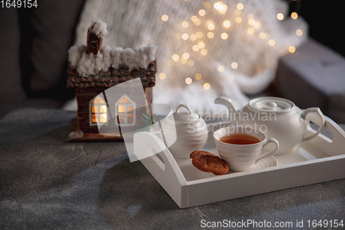 Image of White wooden tray with tea set and miniature of house isolated on grey and white background.