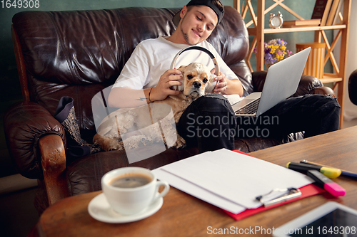 Image of Young man playing with his dog pet and listening to music during Coronavirus or Covid-19 quarantine. Lifestyle concept.