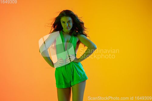 Image of Young beautiful seductive girl in fashionable, summer outfit bright gradient yellow-orange background in neon light