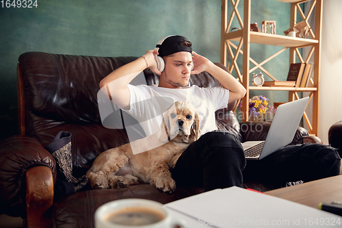 Image of Young man playing with his dog pet and listening to music during Coronavirus or Covid-19 quarantine. Lifestyle concept.