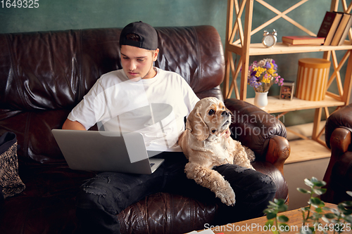 Image of Young man working on laptop computer sitting at home with a dog pet and leaning during Coronavirus or Covid-19 quarantine