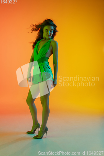 Image of Beautiful seductive girl in fashionable, summer outfit, green jumpsuit on bright gradient yellow-orange background in neon light