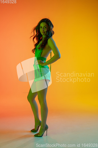 Image of Beautiful seductive girl in fashionable, summer outfit, green jumpsuit on bright gradient yellow-orange background in neon light
