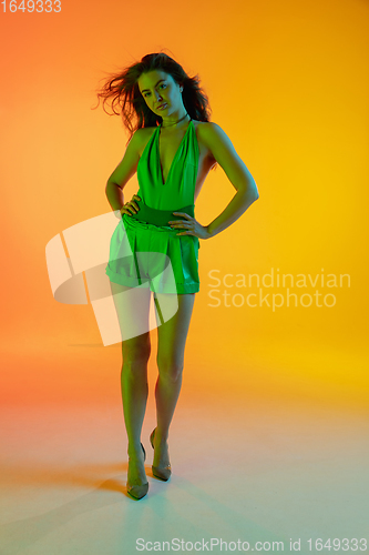 Image of Beautiful seductive girl in fashionable, summer outfit, green jumpsuit on bright gradient yellow-orange background in neon light