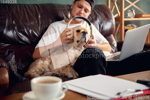 Image of Young man sitting at home with his dog pet and listening to music during Coronavirus or Covid-19 quarantine. Lifestyle concept.