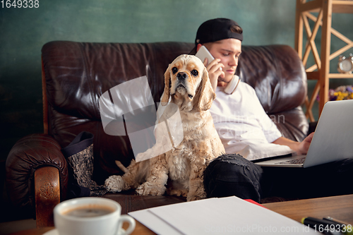 Image of Young man working on laptop computer sitting at home with a dog pet and leaning during Coronavirus or Covid-19 quarantine