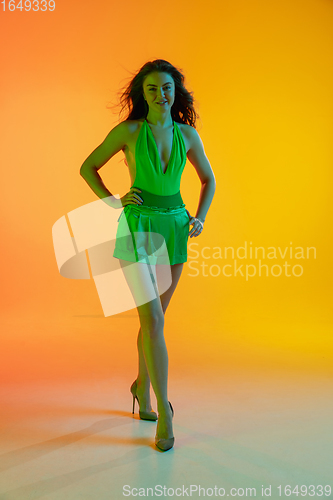 Image of Beautiful seductive girl in fashionable, summer outfit, green jumpsuit on bright gradient yellow-orange background in neon light