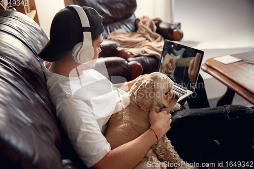 Image of Young man sitting at home with his dog pet and listening to music during Coronavirus or Covid-19 quarantine. Lifestyle concept.