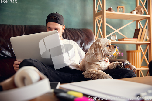 Image of Young man working on laptop computer sitting at home with a dog pet and leaning during Coronavirus or Covid-19 quarantine