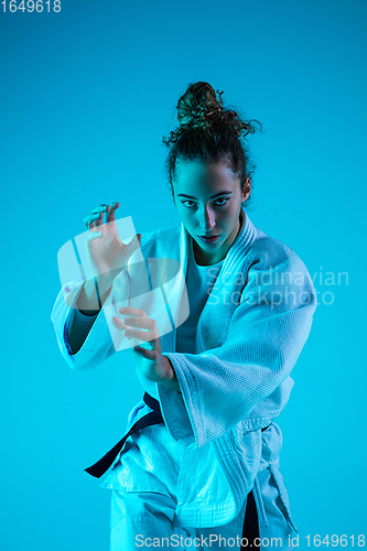 Image of Young girl professional judoist isolated on blue studio background in neon light. Healthy lifestyle, sport concept.