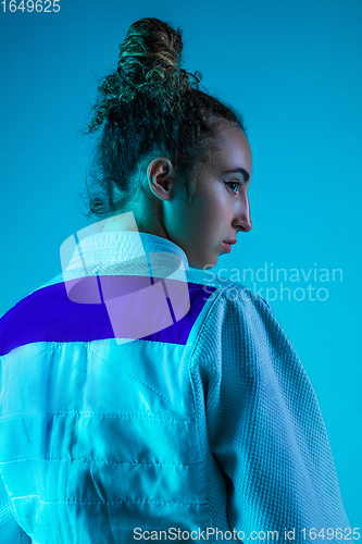 Image of Portrait of professional female judoist isolated on blue studio background in neon light. Healthy lifestyle, sport concept.