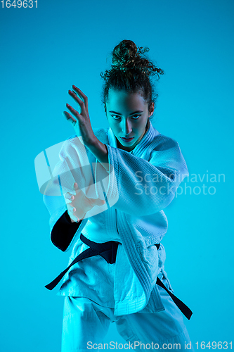 Image of Young girl professional judoist isolated on blue studio background in neon light. Healthy lifestyle, sport concept.