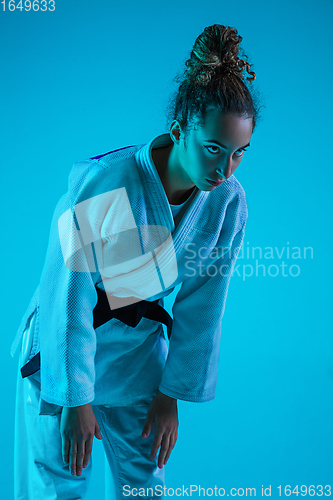 Image of Professional female judoist training isolated on blue studio background in neon light. Healthy lifestyle, sport concept.