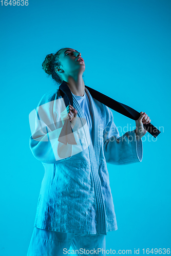 Image of Young girl professional judoist isolated on blue studio background in neon light. Healthy lifestyle, sport concept.
