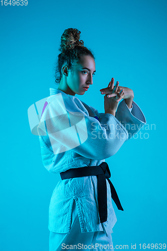 Image of Professional female judoist posing isolated on blue studio background in neon light. Healthy lifestyle, sport concept.