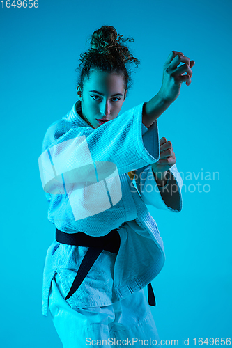 Image of Young girl professional judoist isolated on blue studio background in neon light. Healthy lifestyle, sport concept.