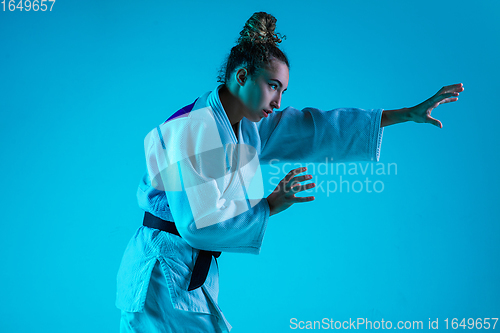 Image of Professional female judoist training isolated on blue studio background in neon light. Healthy lifestyle, sport concept.