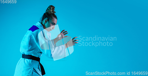 Image of Professional female judoist training isolated on blue studio background in neon light. Healthy lifestyle, sport concept.