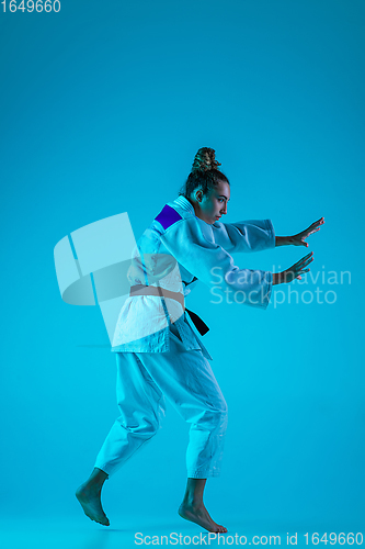 Image of Young girl professional judoist isolated on blue studio background in neon light. Healthy lifestyle, sport concept.