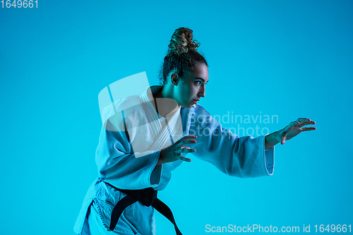 Image of Professional female judoist training isolated on blue studio background in neon light. Healthy lifestyle, sport concept.