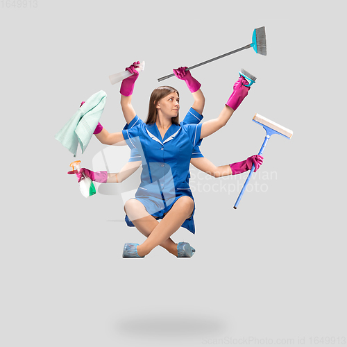 Image of Female housemaid in pink gloves and blue uniform multitask like shiva isolated on gray background. Human emotions.