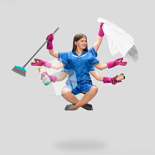 Image of Female housemaid in pink gloves and blue uniform multitask like shiva isolated on gray background. Human emotions.