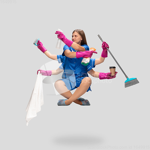 Image of Female housemaid in pink gloves and blue uniform multitask like shiva isolated on gray background. Human emotions.