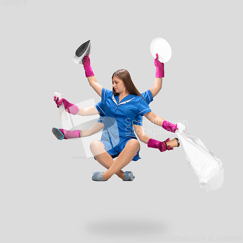 Image of Young woman housemaid, cleaning worker in blue uniform multitask like shiva isolated on gray background.