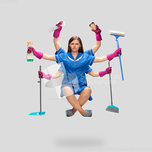 Image of Female housemaid in pink gloves and blue uniform multitask like shiva isolated on gray background. Human emotions.