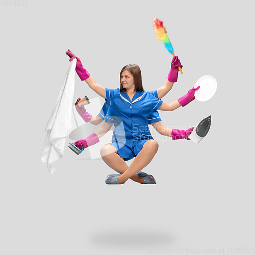 Image of Female housemaid in pink gloves and blue uniform multitask like shiva isolated on gray background. Human emotions.