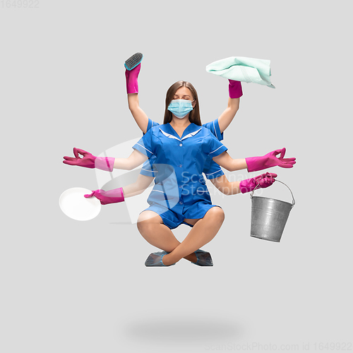 Image of Female housemaid in pink gloves and blue uniform multitask like shiva isolated on gray background. Safety during COVID-19