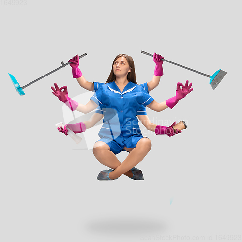 Image of Young woman housemaid, cleaning worker in blue uniform multitask like shiva isolated on gray background.