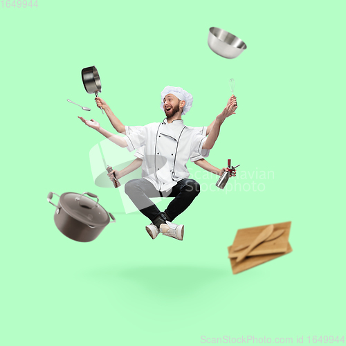 Image of Happy handsome multi-armed chief-cooker levitating isolated on green studio background with equipment