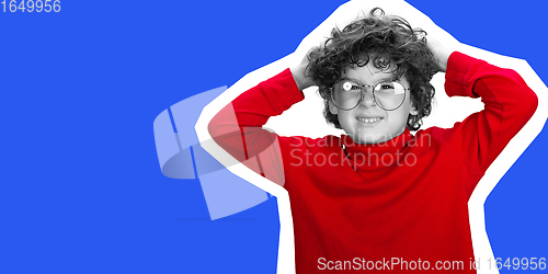Image of Portrait of young curly boy in red wear on blue studio background. Magazine style concept.