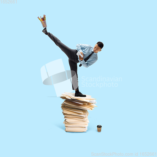 Image of Office worker, businessman, sportsman fighting with deadlines standing on the bunch of documents