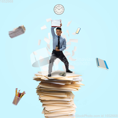 Image of Office worker, businessman, sportsman fighting with deadlines standing on the bunch of documents