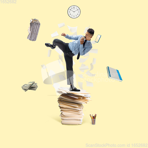 Image of Office worker, businessman, sportsman fighting with deadlines standing on the bunch of documents