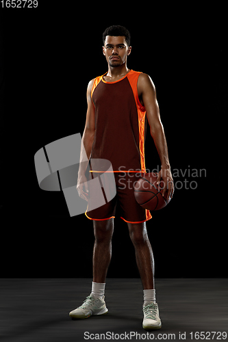 Image of Young african basketball player training on black studio background.