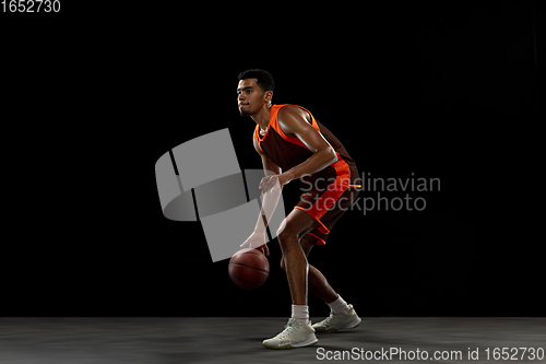 Image of Young african basketball player training on black studio background.