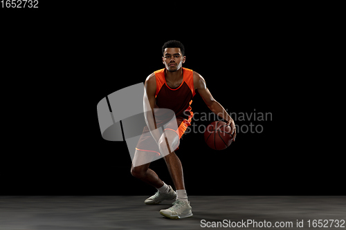 Image of Young african basketball player training on black studio background.