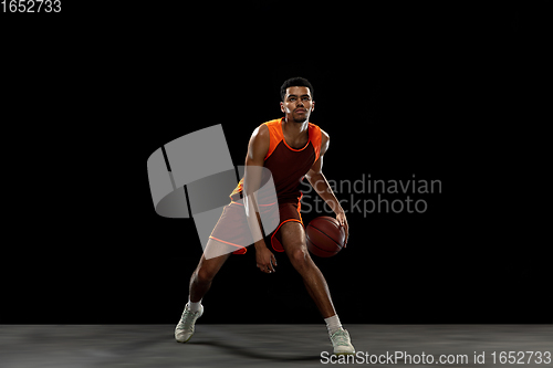 Image of Young african basketball player training on black studio background.